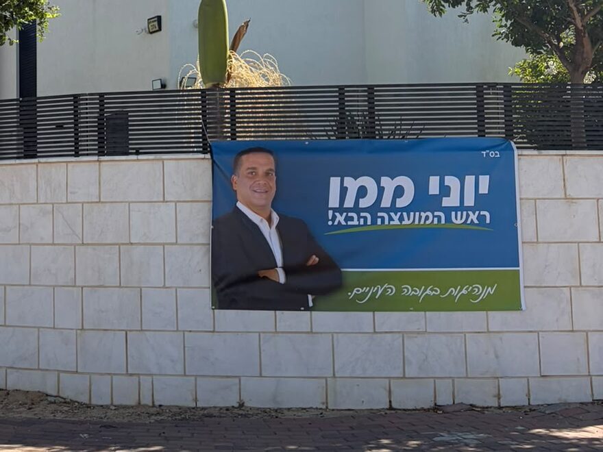 שלט של יוני ממו תלוי על קיר חצר של בית
